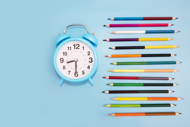 Lápices de colores y un despertador sobre un fondo azul. Concepto de escuela. De vuelta a la escuela.