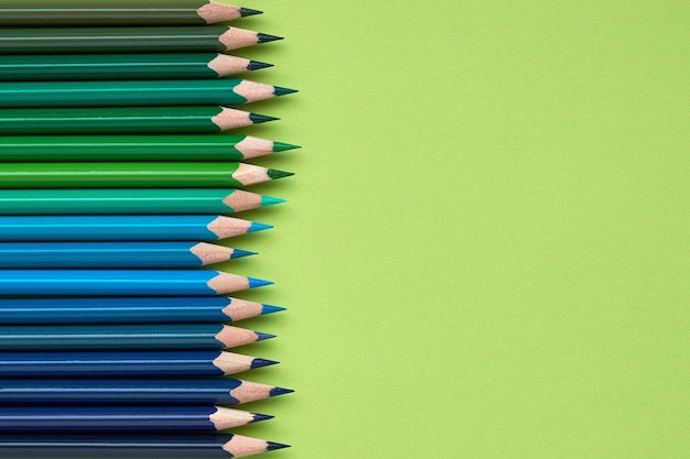 Lápices de colores en una fila sobre fondo verde claro