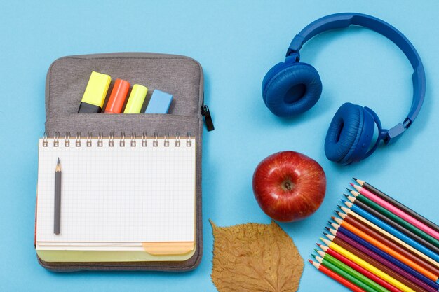 Lápices de colores, manzana, auriculares, cuaderno abierto en estuche-estuche con rotuladores y rotulador.