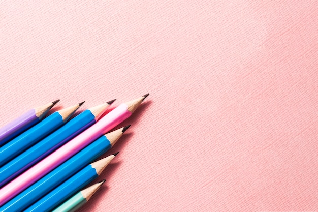 Lápices de colores sobre un fondo rosa pastel.