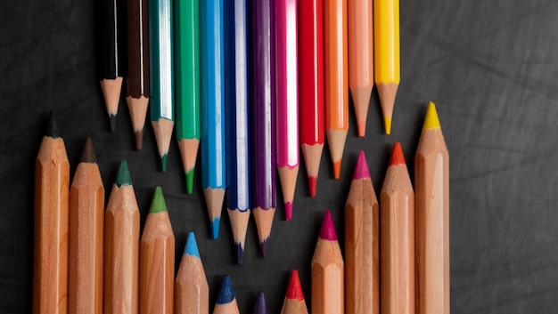 Lápices de madera de diferentes colores sobre fondo de pizarra negra