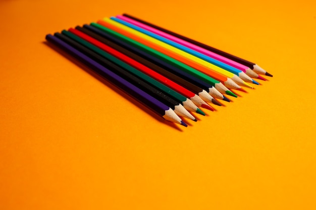Lápices multicolores para dibujar apilados sobre un fondo naranja. Artículos de papelería