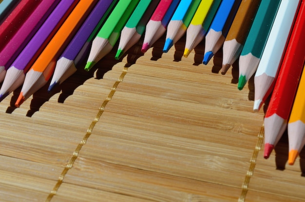 Lápices multicolores dispuestos en arco sobre un fondo de paja.
