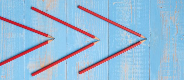 Lápices rojos de forma de flecha sobre fondo azul de madera.