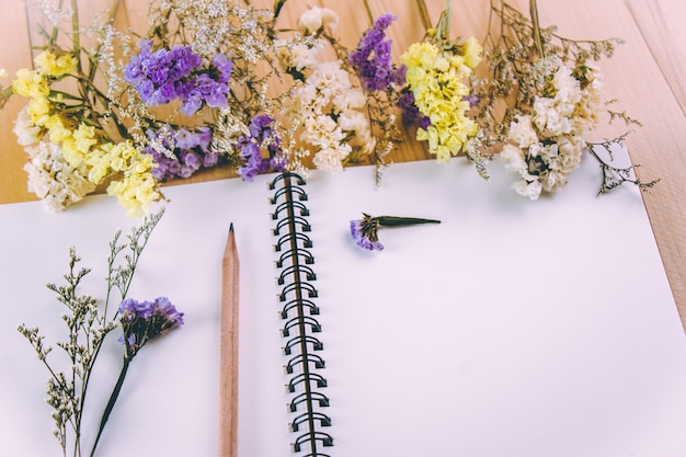 Lápis colocar caderno em branco perto de monte de flor flor, na mesa de madeira