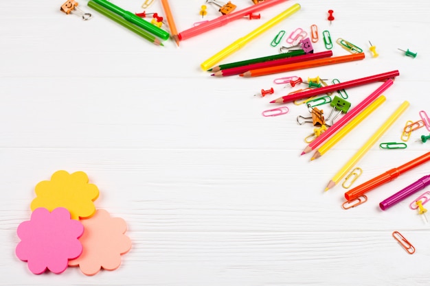 Lápis coloridos e canetas com ponta de feltro, papel para cartas e artigos de papelaria no fundo de madeira branco.