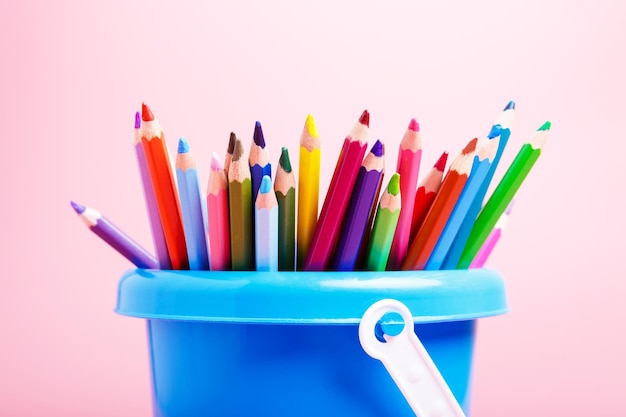 Lápis de cor em um balde azul em um conceito de fundo rosa de aulas de desenho ou hobby para crianças