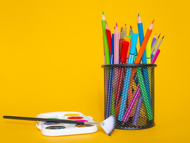 Lápis de cor em uma caixa de lápis em um fundo amarelo com uma folha de papel branca e tintas