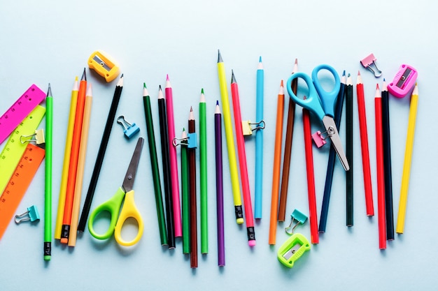 Lápis de cor, tesoura, caderno, régua, caneta, borracha, apontador e muito mais em vidro, papelaria de escola e escritório sobre fundo azul claro.