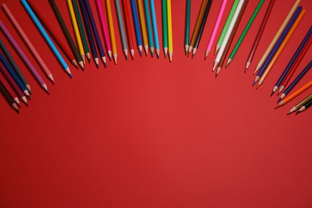 Lápis de madeira coloridos espalhados no conceito de educação de fundo vermelho