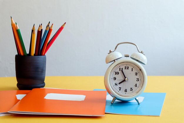 Lápis multicoloridos de volta à escola em um caderno de xícara um despertador em uma mesa em um espaço de fundo cinza para texto