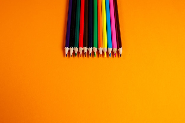 Lápis multicoloridos para desenho empilhados em um fundo laranja. Artigos de papelaria