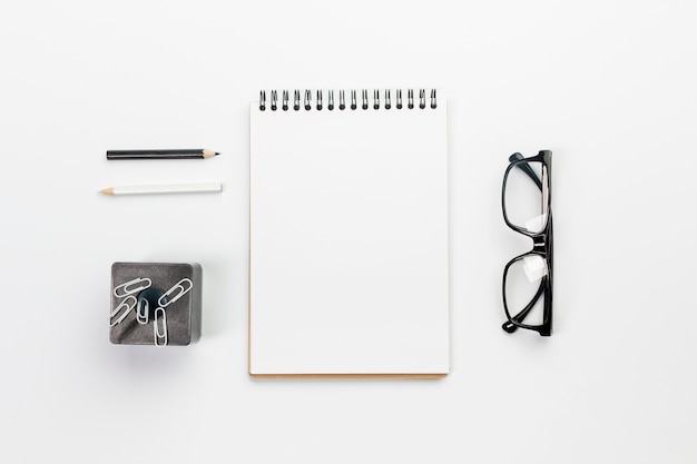 Foto lápis preto e branco com o bloco de notas espiral em branco, clipes de papel no ímã com óculos na mesa de escritório