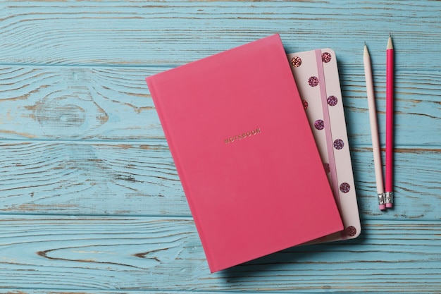 Lápis rosa com caderno em um fundo azul de madeira. Lugar para texto