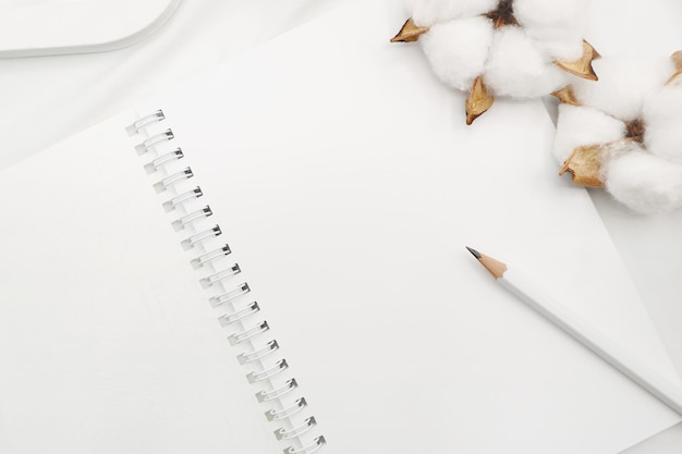 Lápiz blanco en un cuaderno espiral blanco en blanco con flores de algodón en una sábana blanca