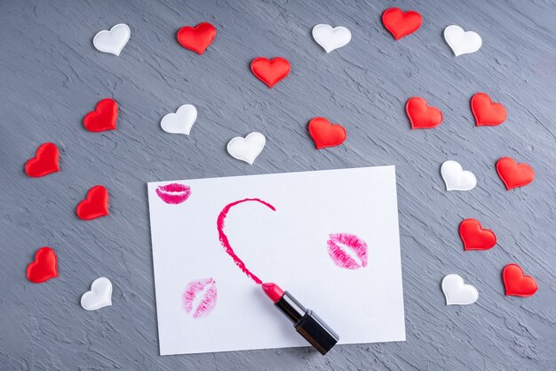 Lápiz labial dibuja en forma de medio corazón sobre papel blanco con besos de lápiz labial sobre un fondo de madera gris