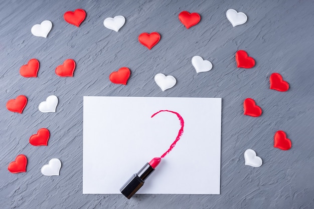 Lápiz labial dibuja en forma de medio corazón sobre papel blanco sobre un fondo de madera gris