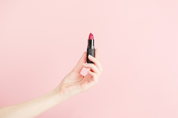 Lápiz labial de explotación de mano femenina. Equipo para maquillage. Maquillaje y visagista. Lugar para texto o diseño creativo. Estilo de maqueta. Concepto de cosmética y belleza. Aislado en rosa.