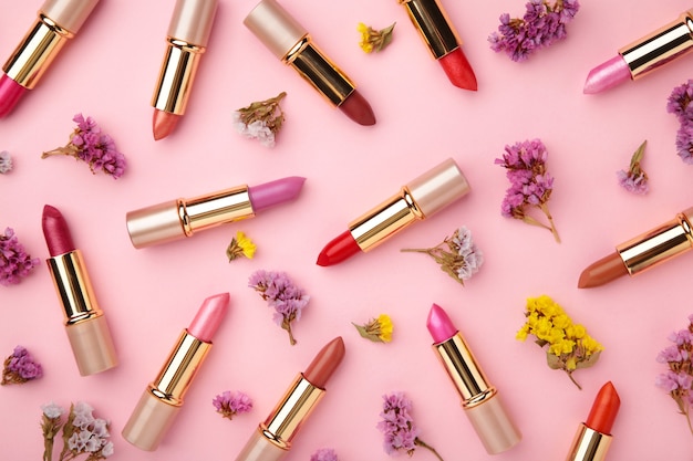 Lápiz labial con hermosas flores en mesa rosa. Vista superior