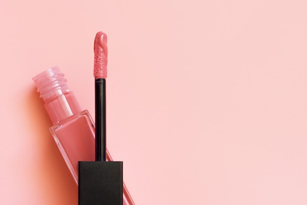 Lápiz labial líquido y aplicador sobre superficie rosa