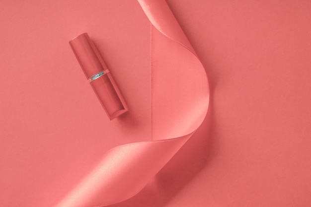 Lápiz labial de lujo y cinta de seda sobre fondo de vacaciones de coral maquillaje y cosméticos flatlay para el diseño de productos de marca de belleza