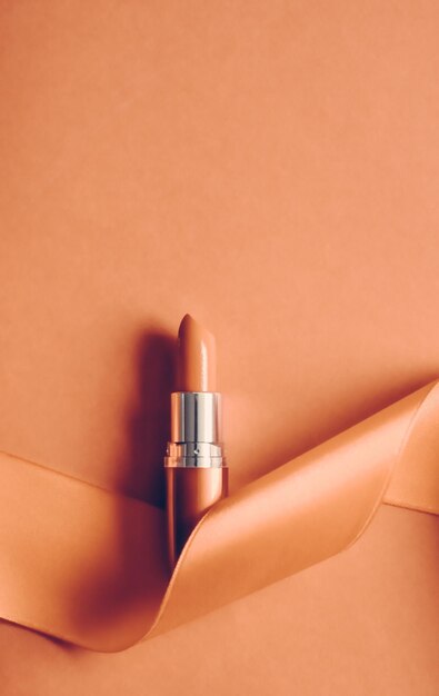 Lápiz labial de lujo y cinta de seda sobre fondo de vacaciones naranja maquillaje y cosméticos flatlay para el diseño de productos de marca de belleza