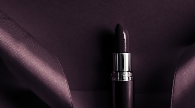Lápiz labial de lujo y cinta de seda sobre maquillaje de fondo de vacaciones de color púrpura oscuro y flatlay de cosméticos para el diseño de productos de marca de belleza