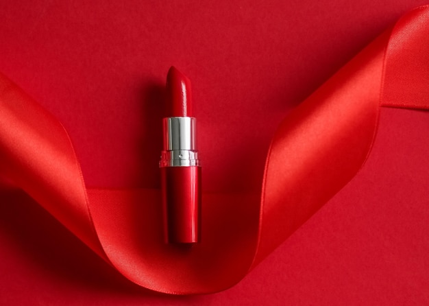 Lápiz labial de lujo y cinta de seda sobre maquillaje de fondo de vacaciones rojo y flatlay de cosméticos para el diseño de productos de marca de belleza