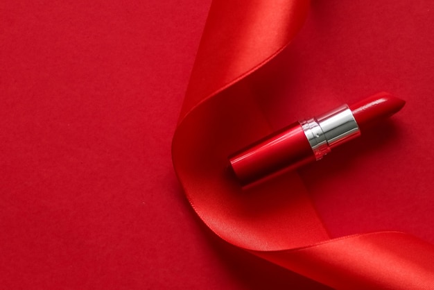 Lápiz labial de lujo y cinta de seda sobre maquillaje de fondo de vacaciones rojo y flatlay de cosméticos para el diseño de productos de marca de belleza
