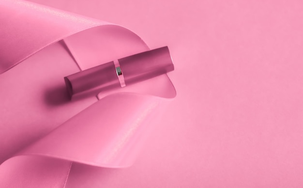 Lápiz labial de lujo y cinta de seda sobre maquillaje de fondo de vacaciones rosa y flatlay de cosméticos para el diseño de productos de marca de belleza