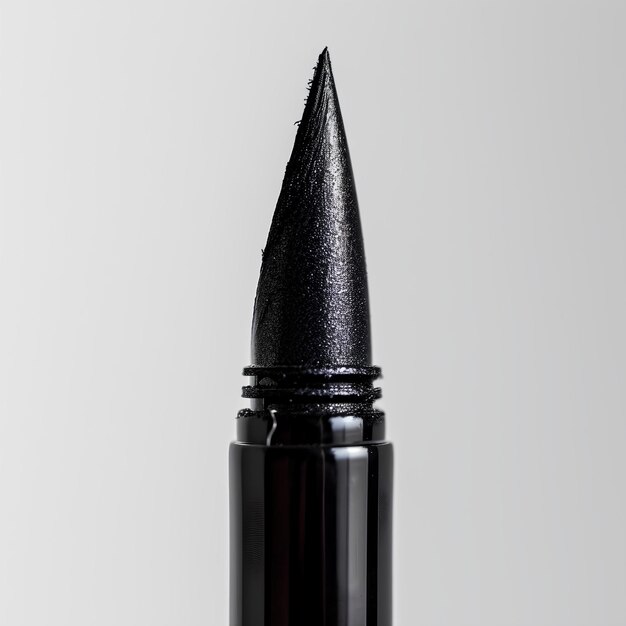 Un lápiz labial negro con una punta negra en un fondo blanco con una botella negra de lápiz lipstick en la parte delantera