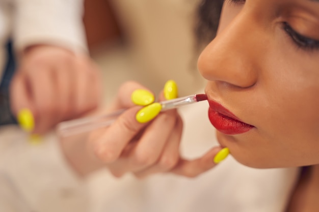 El lápiz labial rojo se aplica cuidadosamente por un experto visagiste con un cepillo de labios profesional