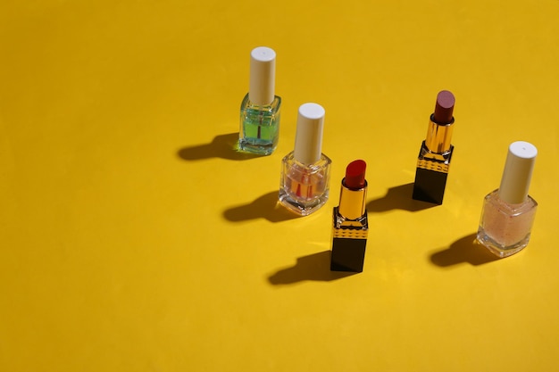 Lápiz labial rojo ftv botellas de esmalte de uñas sobre fondo amarillo con sombras Bodegón de belleza