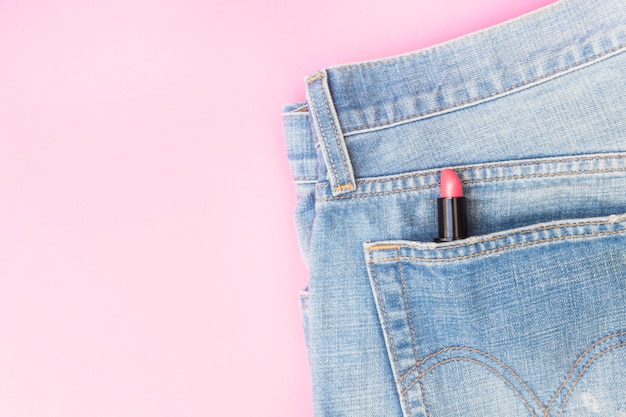 Lápiz labial rosa en el bolsillo de los pantalones vaqueros sobre fondo rosa