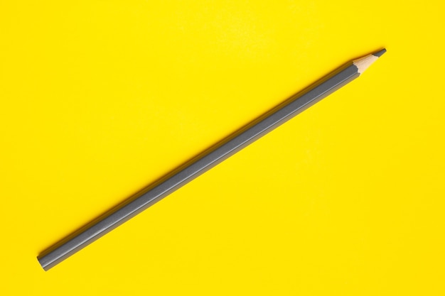 Lápiz de madera afilado gris diagonal sobre un fondo amarillo brillante, aislado, espacio de copia, maqueta