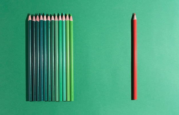 Un lápiz rojo se encuentra frente a varios verdes sobre un fondo verde.
