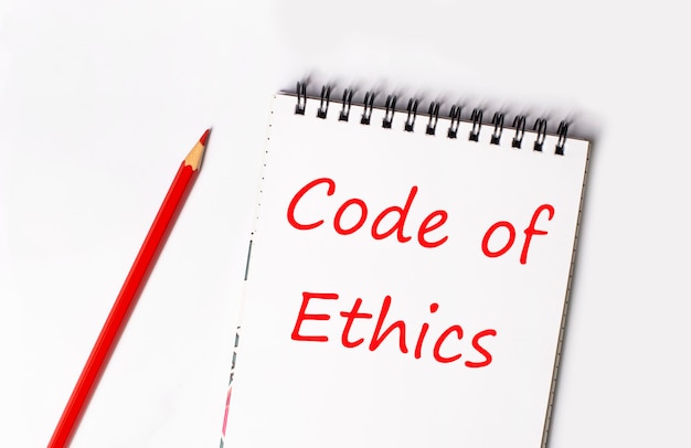 Foto lápiz rojo y libreta blanca con el texto código de ética sobre un fondo claro