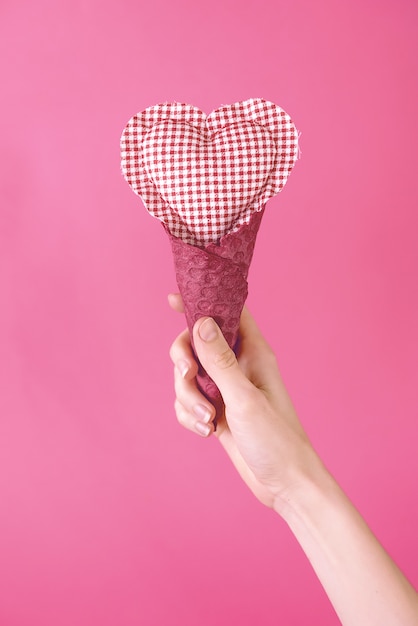 Lappenherz in einer Waffelschale in einer Hand auf einem rosa Hintergrund