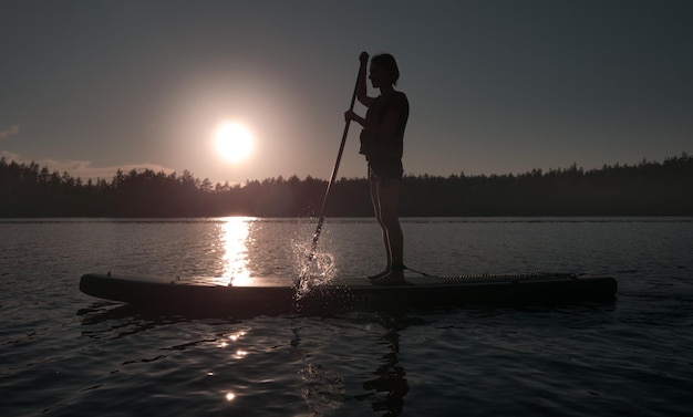 Lappenranta Finlandia 7 de junio de 2022 Silueta de una surfista SUP en una tabla de remo a la luz del cielo del atardecer Tema de recreación activa y estilo de vida saludable