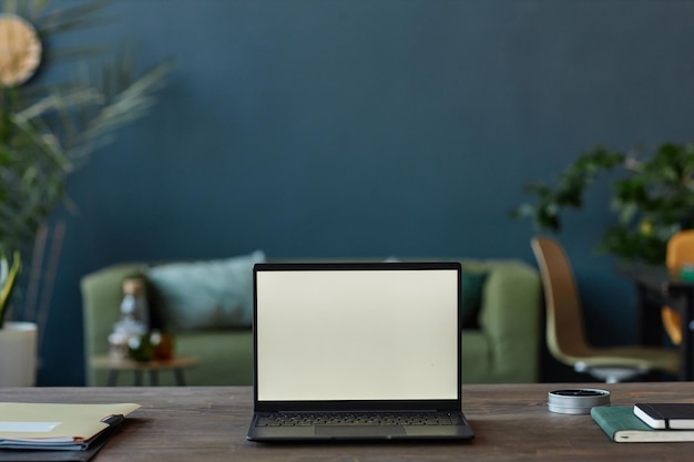 Laptop abierto en la mesa en la oficina con pantalla en blanco en la pared azul azul
