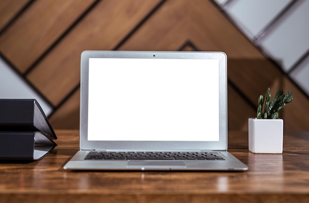 Laptop-Bildschirm verspotten weiße Anzeigeschablone auf silbernem Computer auf hölzernem Schreibtischtisch mit Pflanzenordnern
