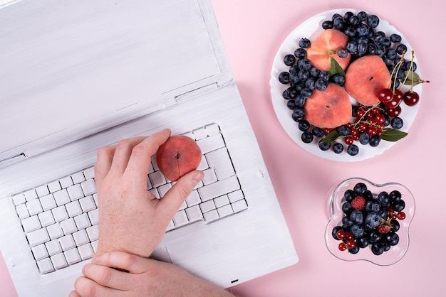 Laptop blanca creativa sobre fondo rosa de moda con almuerzo de frutas de verano en la oficina