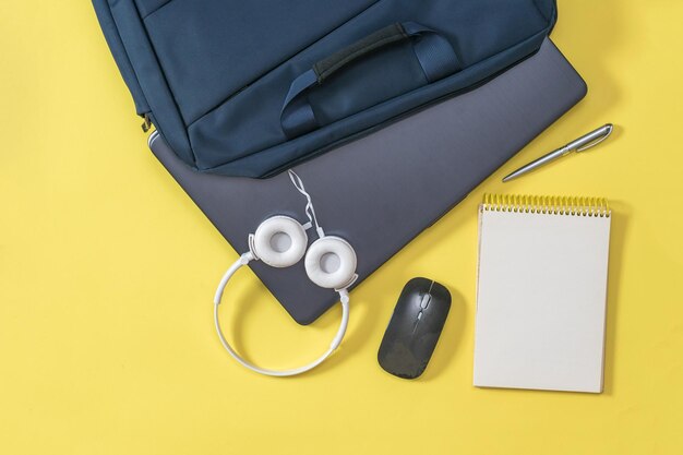 Laptop, bloco de notas e fones de ouvido brancos com uma bolsa em um fundo amarelo. Acessórios para estudo, negócios e trabalho.