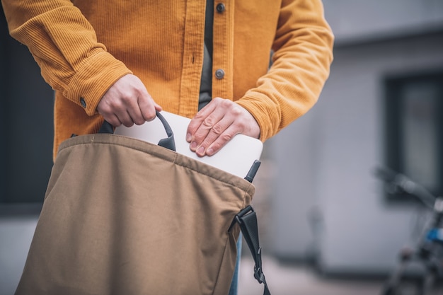 Laptop en bolsa. Cerca de la mano del hombre poniendo el portátil en una bolsa