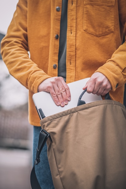 Laptop en bolsa. Cerca de la mano del hombre poniendo el portátil en una bolsa