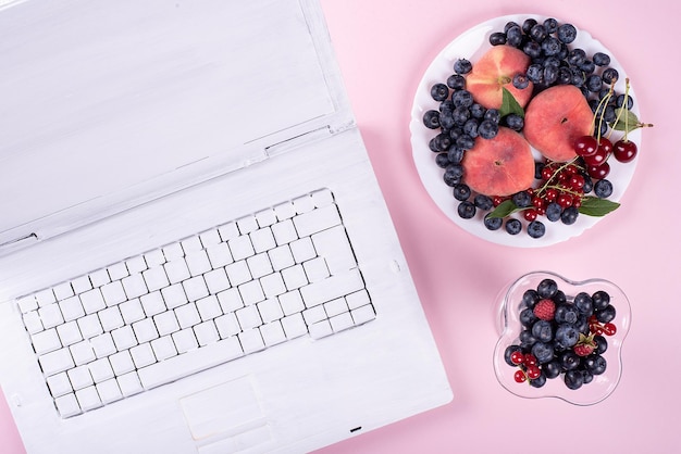 Laptop branco criativo sobre fundo rosa na moda com almoço de frutas de verão no escritório