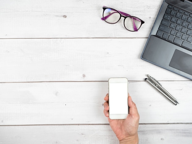 Laptop-Brille Kaffeetasse und zwei silberne Stift Büroarbeitsplatz Draufsicht und Hand halten Smartphone