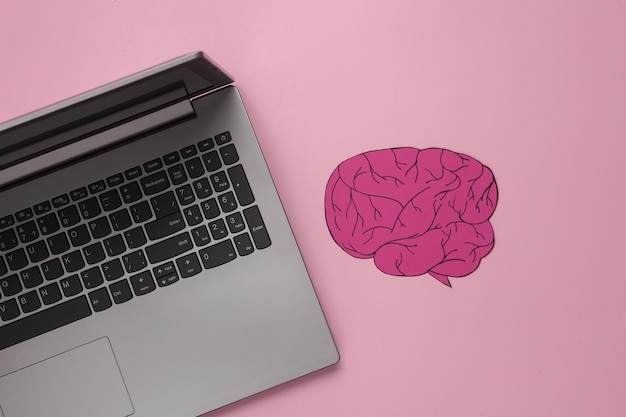 Laptop con cerebro de papel sobre un fondo rosado