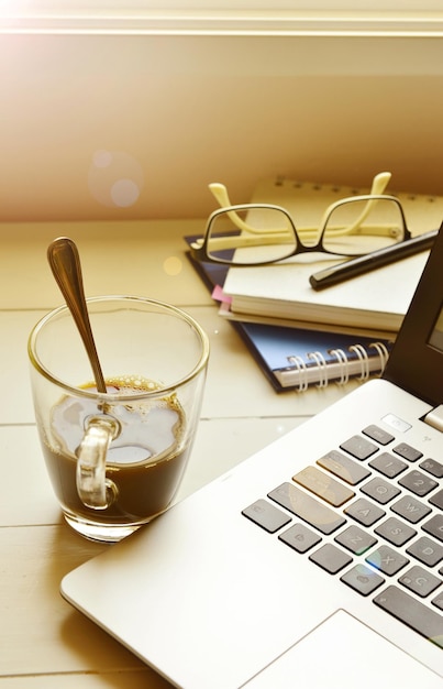 Laptop com café preto e óculos em diário em espiral mantido em mesa de madeira