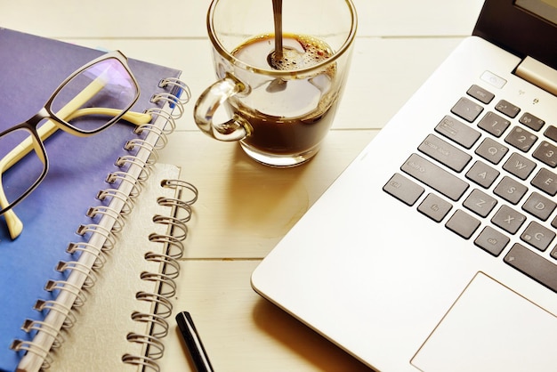 Laptop com café preto e óculos em diário em espiral mantido em mesa de madeira